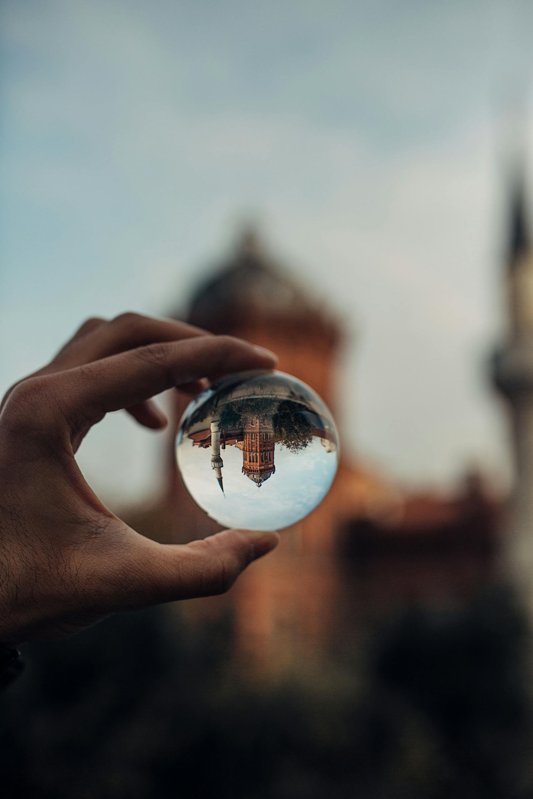 A hand holds a lensball capturing an inverted historic building in Istanbul, creating a dreamy effect.
