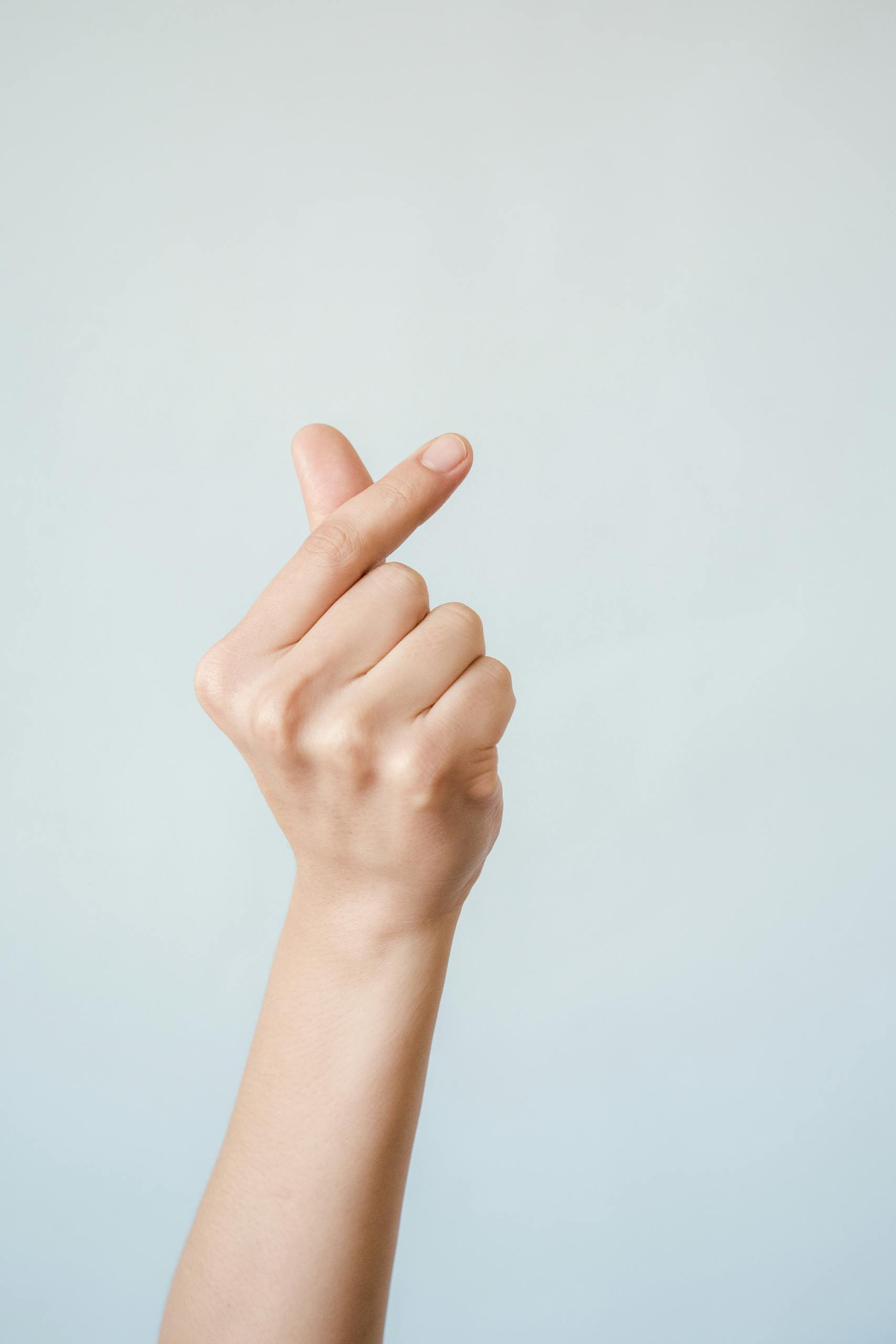 Close-up of a hand making a heart gesture, captured in a minimalist style with a soft background.